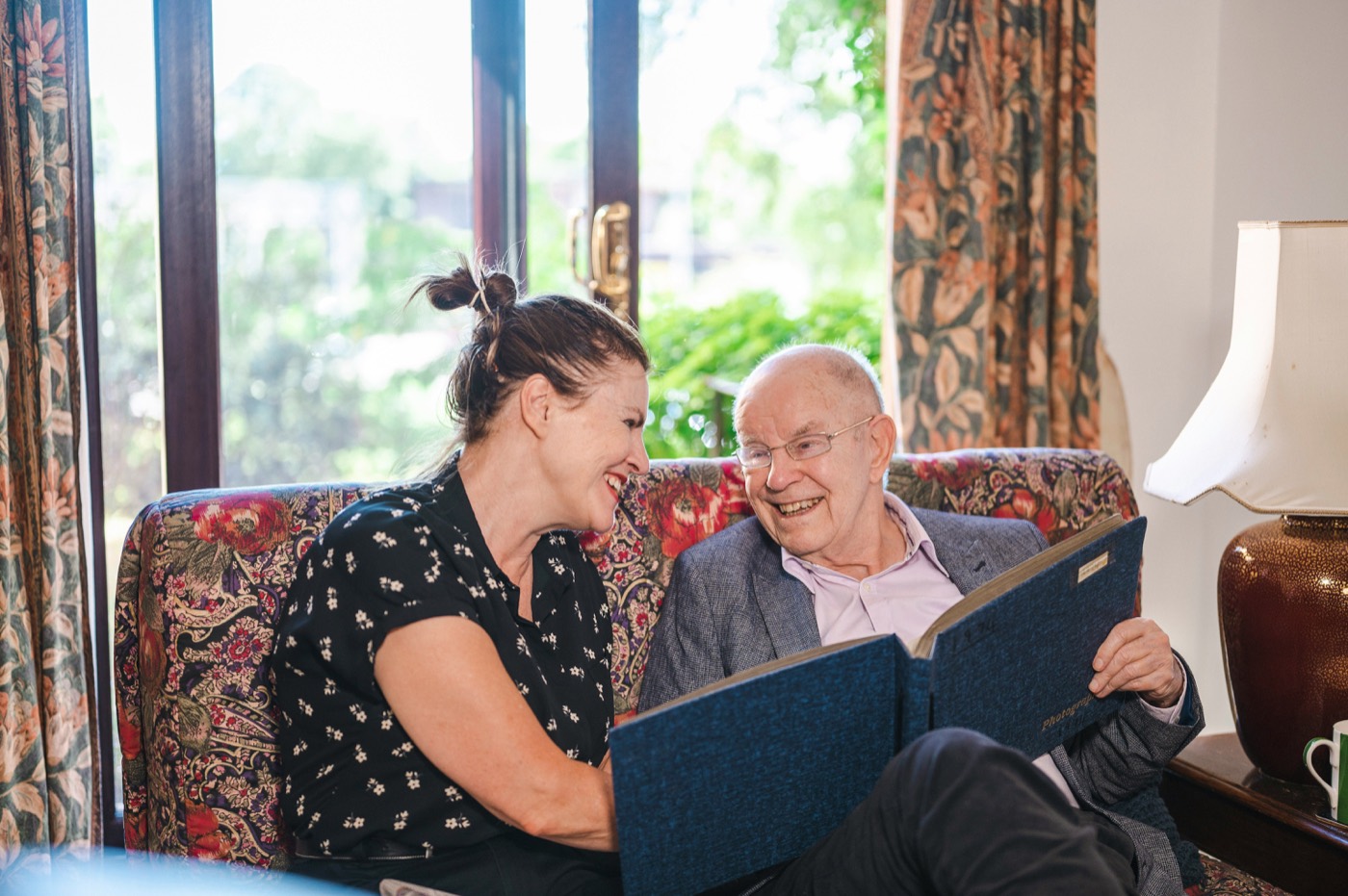 A support worker and an older man laughing together over a photo album at home