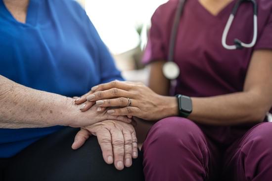 A caregiver's hand resting reassuringly on an older person's hands